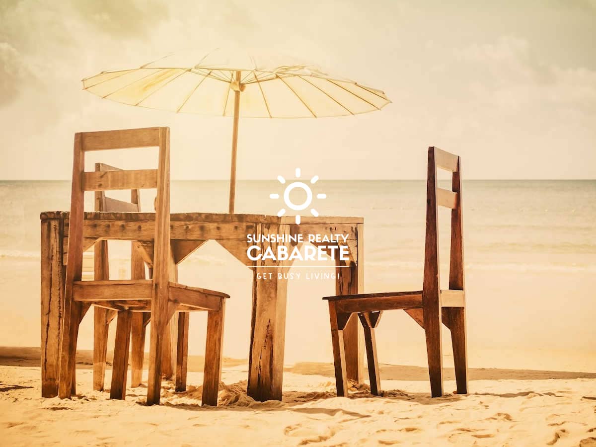 Image of a wooden table with two chairs in the sand at the edge of the beach